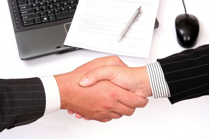 man and woman shaking hands in front of laptop and signed contract