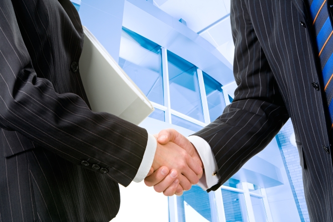 Two partners shaking hands at meeting in front of building